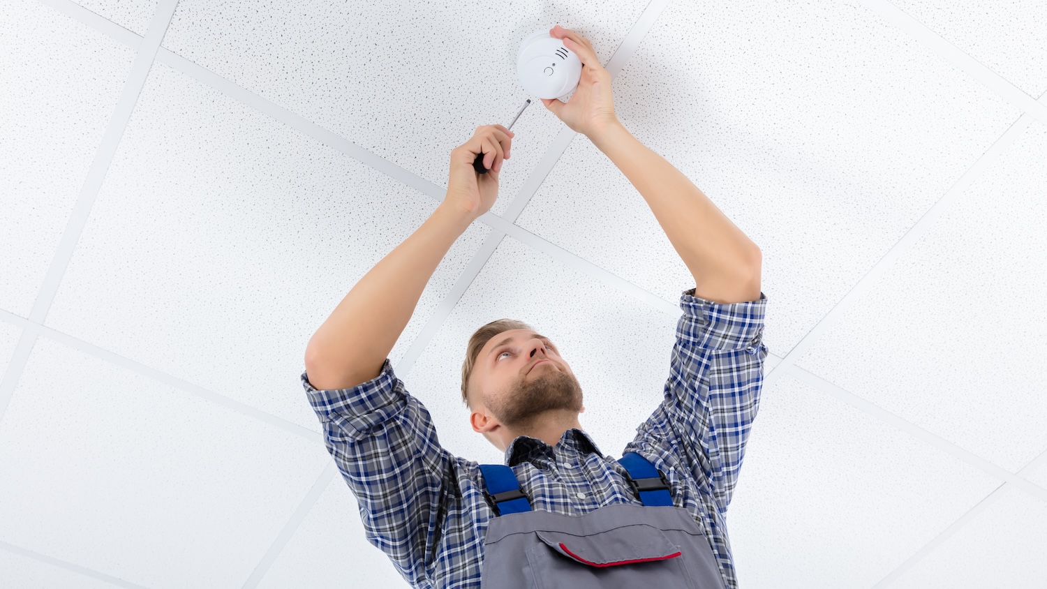 Image of an electrician checking a smoke detector for Honeywell smoke detectors story